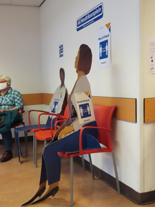 850672 Afbeelding van kartonnen poppen en een patiënt in de wachtruimte van de afdeling cardiologie van het ...